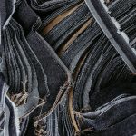 Close-up de tiras sobrepostas de tecido jeans em diferentes tons de azul, destacando suas texturas.