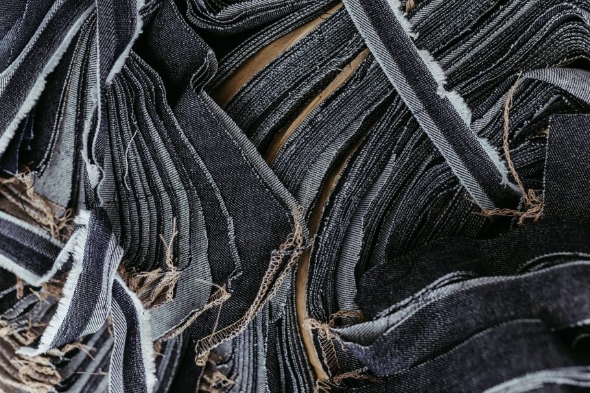 Close-up de tiras sobrepostas de tecido jeans em diferentes tons de azul, destacando suas texturas.