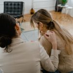 Duas mulheres conversam sentadas em um ambiente interno, em um momento de escuta e apoio mútuo.