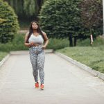 Mulher negra e plus size correndo em um parque, durante atividade física ao ar livre.