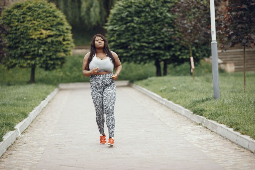 Mulher negra e plus size correndo em um parque, durante atividade física ao ar livre.