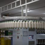 Linha de produção têxtil industrial com máquinas automatizadas e carretéis de fios.