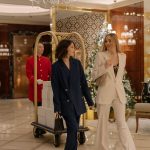 Duas mulheres usando ternos elegantes caminham pelo saguão decorado de um hotel.