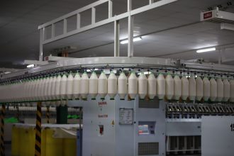 Linha de produção têxtil industrial com máquinas automatizadas e carretéis de fios.