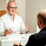 Profissional de saúde conversa com paciente em uma sala de atendimento clínico.