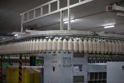 Linha de produção têxtil industrial com máquinas automatizadas e carretéis de fios.