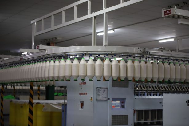 Linha de produção têxtil industrial com máquinas automatizadas e carretéis de fios.